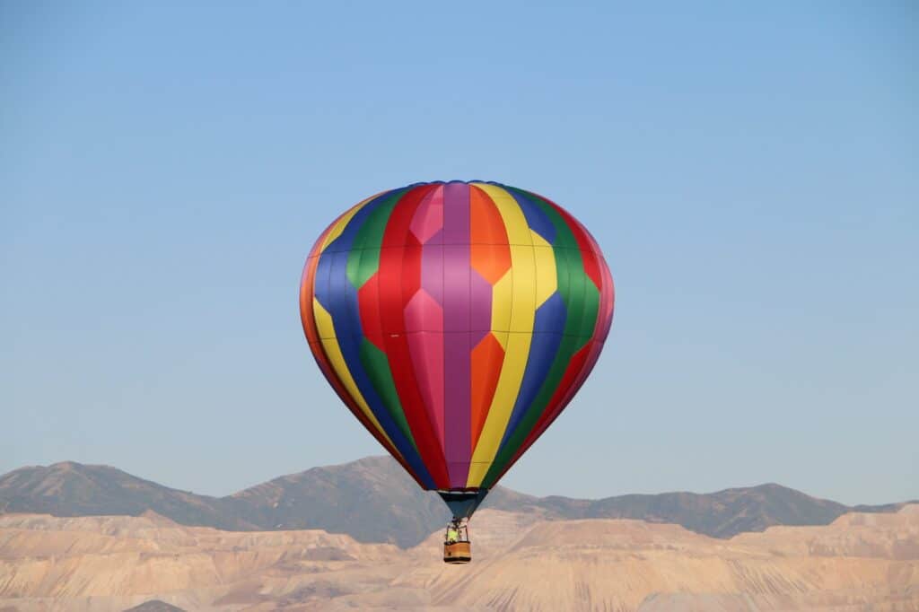 Vibrant colored hot air balloon floating above with Utah’s western mountains in the background.