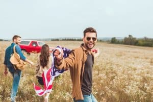 handsome young man with united states flag in flower field with friend during car trip