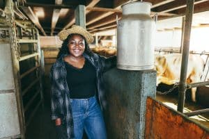 Young african farmer woman holding milk churn inside cowshed - Focus on face