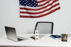 wooden cubes with seo lettering near laptop and american flag in modern office